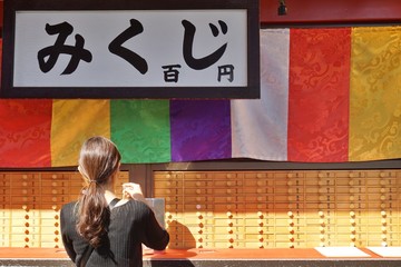 A woman get a OMIKUJI, random fortunes written on paper strips at shrines and Buddhist temples in Japan. The Japanese words means OMIKUJI price 100yen.