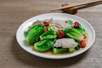 close up of stir fried cabbage sprout with pork in a ceramic dish on wooden table. homemade style food concept.