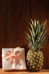 Ripe pineapple with white gift box on wooden background. Healthy food ingredients, tropical fruits, diet, slimming vegan foods, weight loss. Minimal style, front view, vertical social media banner.