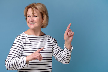 Friendly smiling middle aged woman pointing at copyspace isolated on blue background. Studio shot