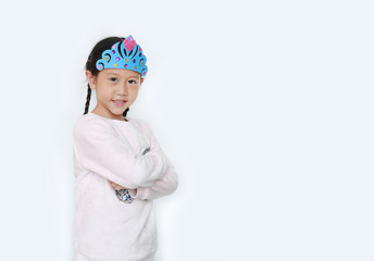 Portrait of confident little Asian child girl with wearing a crown toys and cross one arm isolated over white background with copy space.