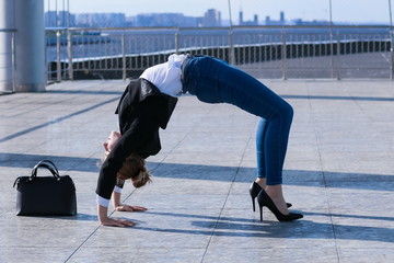 slender young woman in black jacket and jeans practice yoga asana bridge pose during break while working day in office