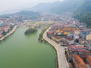 Fototapeta premium Aerial view of Sapa cityscape covered by fog with Sapa lake an iconic emerald green lake in the downtown of Sapa the capital city in Lao Cai province in north-west of Vietnam.