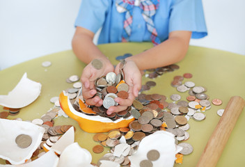 Close-up coins of broken piggy bank in little girl hands on table over white background.