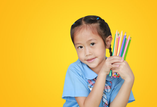 Portrait little girl in school uniform holding color pencils over yellow background. Education and school concept.