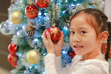 Fototapeta na wymiar Close-up Asian little girl looking and holding christmas ball of christmas tree in the winter season and happy new year festival.