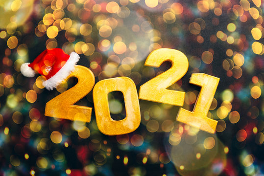 Happy New Year 2021. Golden digits 2021 with christmas hat are on black background with bokeh. Holiday Party Decoration or postcard concept with top view and copy space.