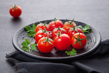 Fresh cherry tomatoes on black round plate,  on dark background.