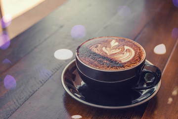 A black cup of coffee with art on a table, bokeh lights