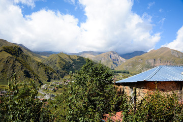 Fototapeta na wymiar Panoramic view to the mountains and Gergeti Trinity Church from Stepantsminda village (Kazbegi) in Georgia