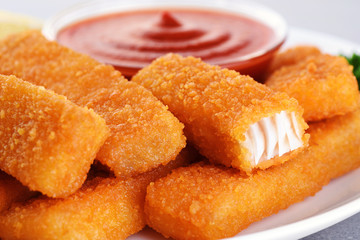 Fish fingers sticks on a plate with parsley, lemon and ketchup.