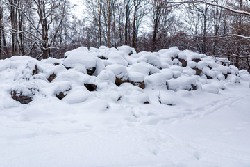 a large pile of stones under the snow lies in the park near the road