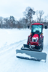 A harvesting tractor is standing in front of snow cleaning in a park on the road, vertical orientation.
