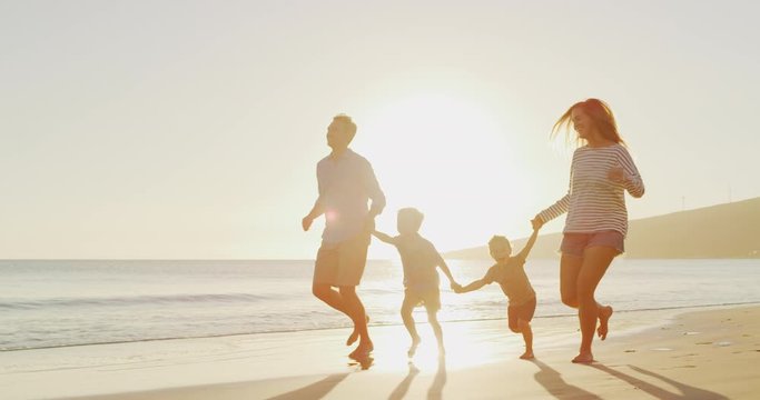 Happy smiling toddler boys holding hands with their parents running together on the beach, happy family silhouette on the beach