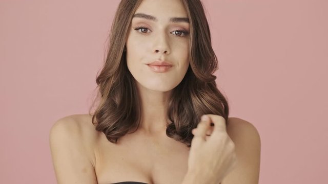 A beautiful young shirtless woman is poising while turning to the camera isolated over pink background