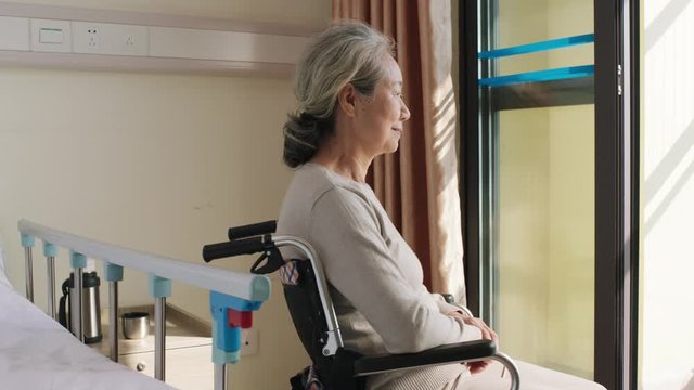 senior asian woman sitting in wheel chair by the window turning to camera smiling