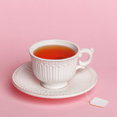 White exquisite porcelain cup with tea bag on a delicate pink background.
