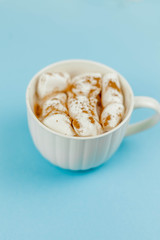 A large white mug with cocoa and marshmallows, cinnamon on a blue background. Christmas motives. Traditional winter drink.