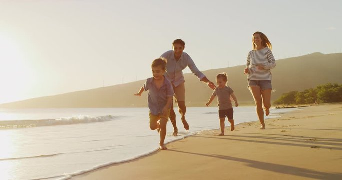 Two happy smiling toddler brothers running in front of their parents on the beach at sunset, happy family on a tropical vacation together