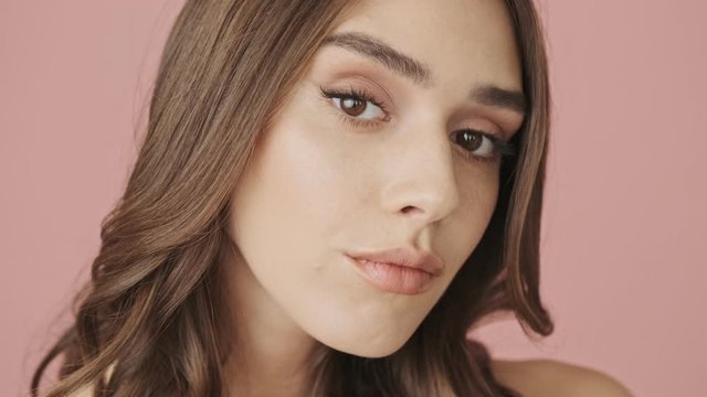 A close-up view of young beautiful woman is raises her brows while looking to the camera isolated over pink background