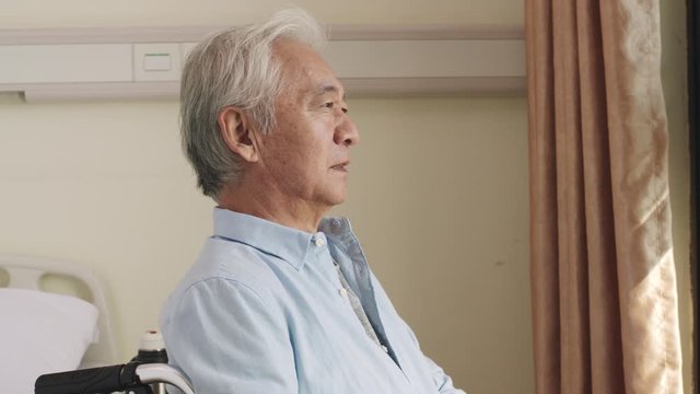 senior asian man sitting in wheel chair by the window turning to camera smiling