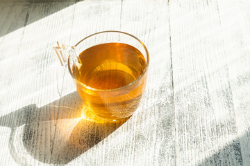 Cup of herbal tea on wooden background. Glass cup. Rays of sunlight