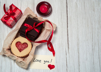 The Concept Of Valentine's Day. A note with a Declaration of love, a box of chocolate and cookies in the form of hearts, a candle and a decorative gift box on a light wooden background.