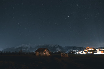 Wooden Hut With Snow Mountains In The Background At Night Time.