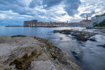 Sunset and Night view of Dubrovnik old town from seaside with reefs in foreground, Croatia