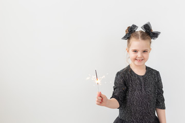 Holidays, christmas and new year concept - Happy child holds burning sparkler in her hand over white background with copy space