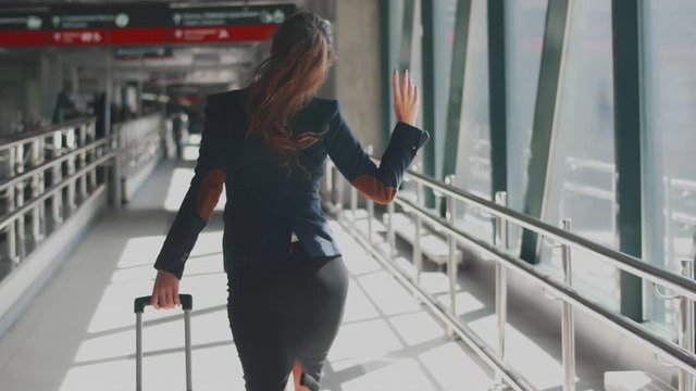 Happy and excited woman in formal wear with luggage dancing while walking in airport