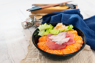 Japanese Chirashi made with assortment of three raw fishes, salmon, tuna and cod fish served on white vinegary rice with Wasabi sauce and ginger slices on top in a bowl.