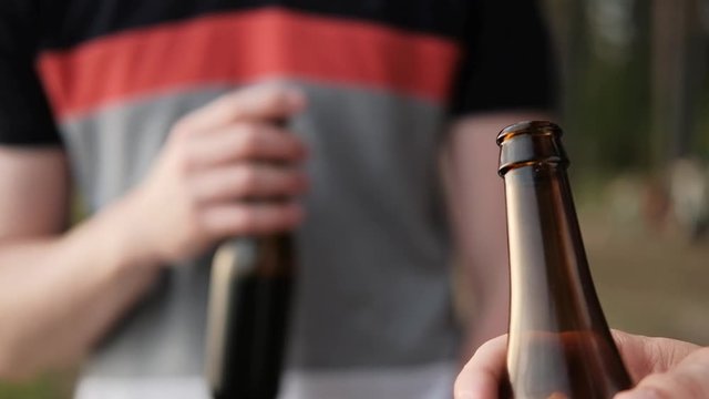 Two young men drink beer from bottles and relax outdoors. A weekend in nature, a meeting of friends and party in the woods.