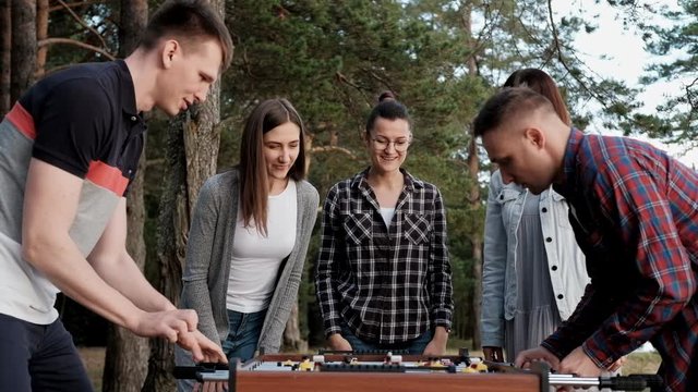 Friends play table football or kicker outdoors. A party in nature. Players and fans rejoice in the victory.