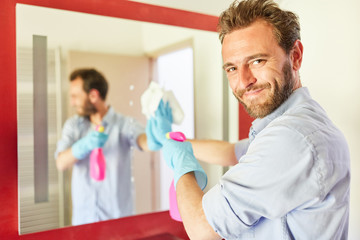 Hausmann mit Putztuch beim Spiegel putzen