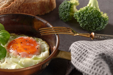 Fried egg in a frying pan with bacon and bread for breakfast on dark background, decorated valerian...