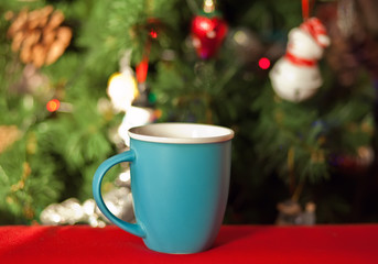 Blue cup of coffee or tea nearby Christmas tree