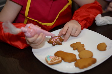 Girl decorates Christmas gingerbread cookies using pink glaze