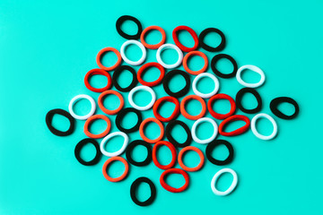 A scattering of multi colored elastic bands for hair of scarlet, red, white, brown and black colors on a blue turquoise background. The concept of girlish things for beauty and creating hairstyles