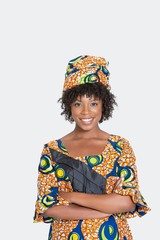 Portrait of young woman in African print attire standing arms crossed over gray background