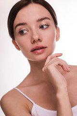 Vertical picture of young woman with clear pure and nice face skin. Posing on camera and look down left. Hold hand under chin. Slim well-built woman. Glowing skin with make-up on. Isolated.