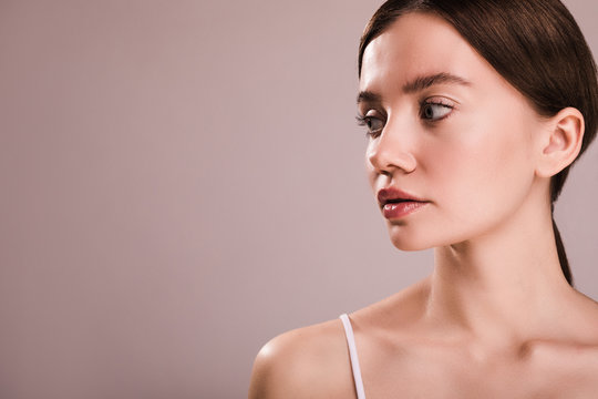 Calm peaceful young woman loook to left. Side view. Natural beauty. Glowing clear and clean skin. Isolated over beige background.