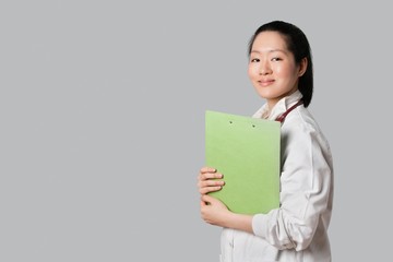 Portrait of a confident Asian female doctor holding clipboard over gray background