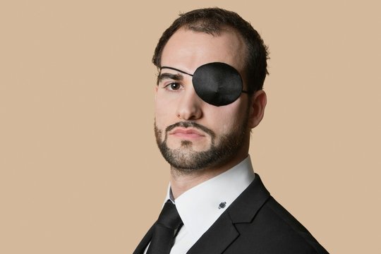 Portrait of a young businessman with eye patch over colored background