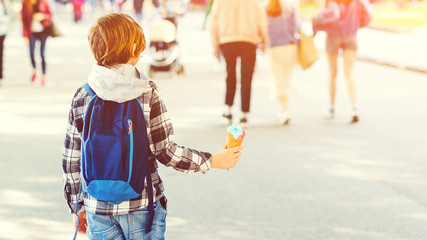 Schoolboy walking on crowded street in the center of the city and eating ice-cream. Stylish kid with backpack walking outdoors