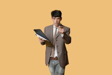 Portrait of a young businessman pointing while holding clipboard over colored background
