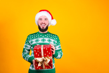 Studio portrait of handsome bearded man wearing christmas sweater with snowflake ornament, posing over the yellow wall, copy space for text. Festive background. Male with facial hair smiling.