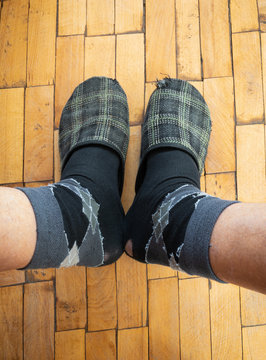 Top view on male legs wearing old worm socks and slippers standing on old parquetry