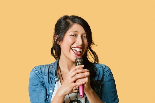 Portrait Of A Young Woman Singing Into A Hairbrush Over Colored Background