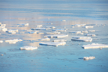 Ice floes illuminated by the sun on the surface of a large reservoir. Vast blue space. Arctic sea